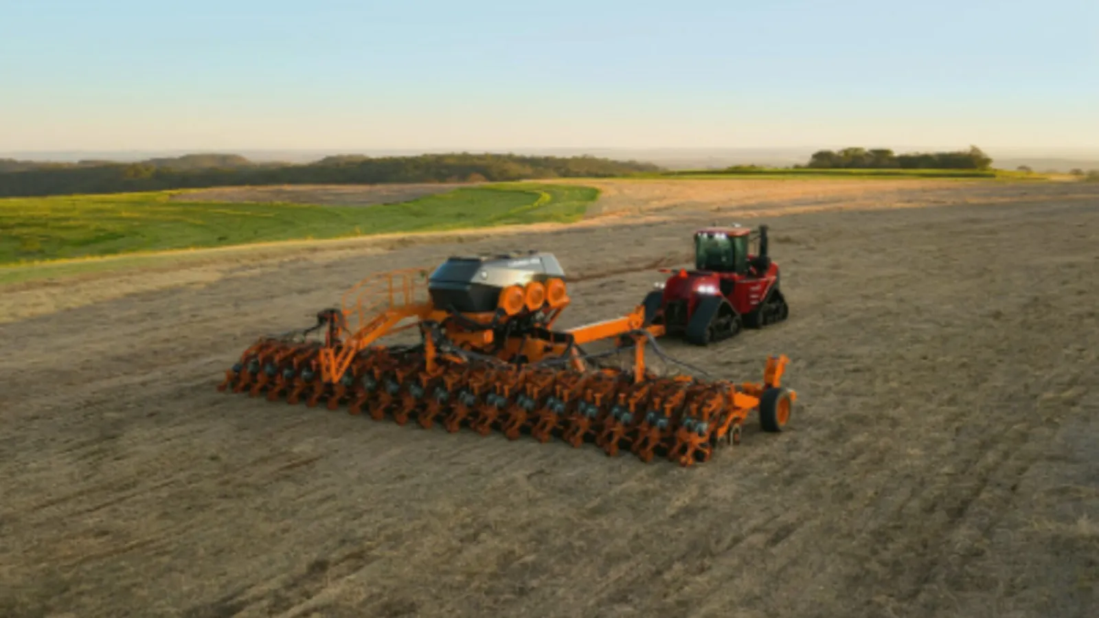 Tractor agrícola arrastrando una sembradora directa de gran anchura sobre rastrojo al atardecer