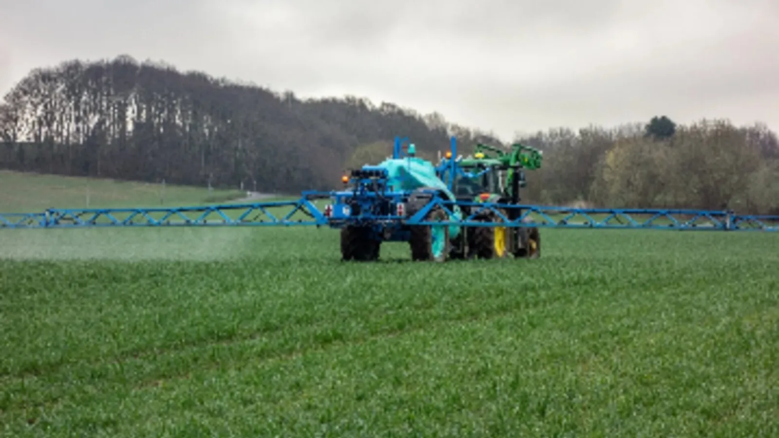 Tractor con barra pulverizadora aplicando fertilizante líquido sobre un campo de cereal verde