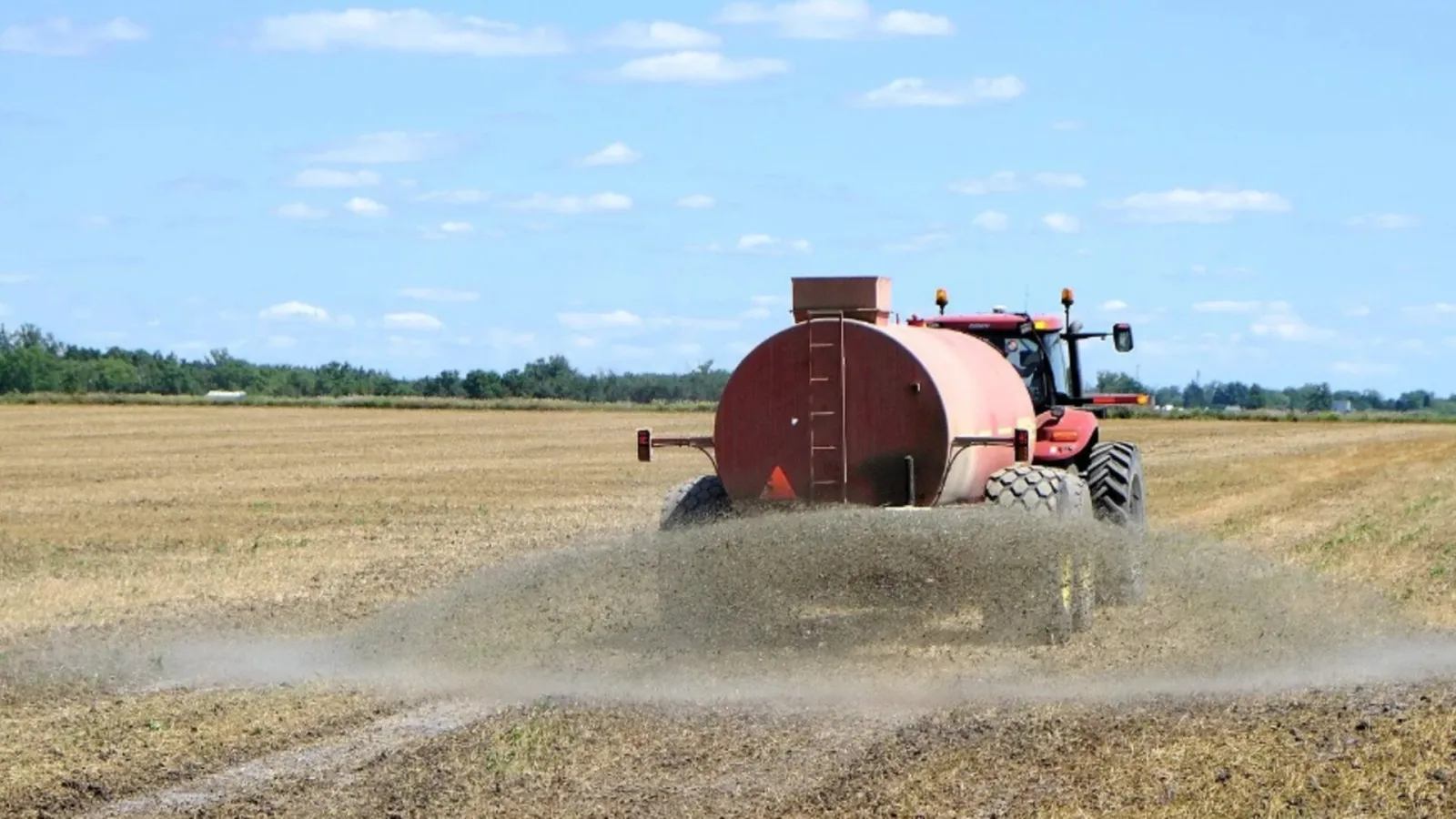 Tractor con cisterna roja aplicando fertilizante nitrogenado sobre un campo de rastrojo bajo cielo despejado