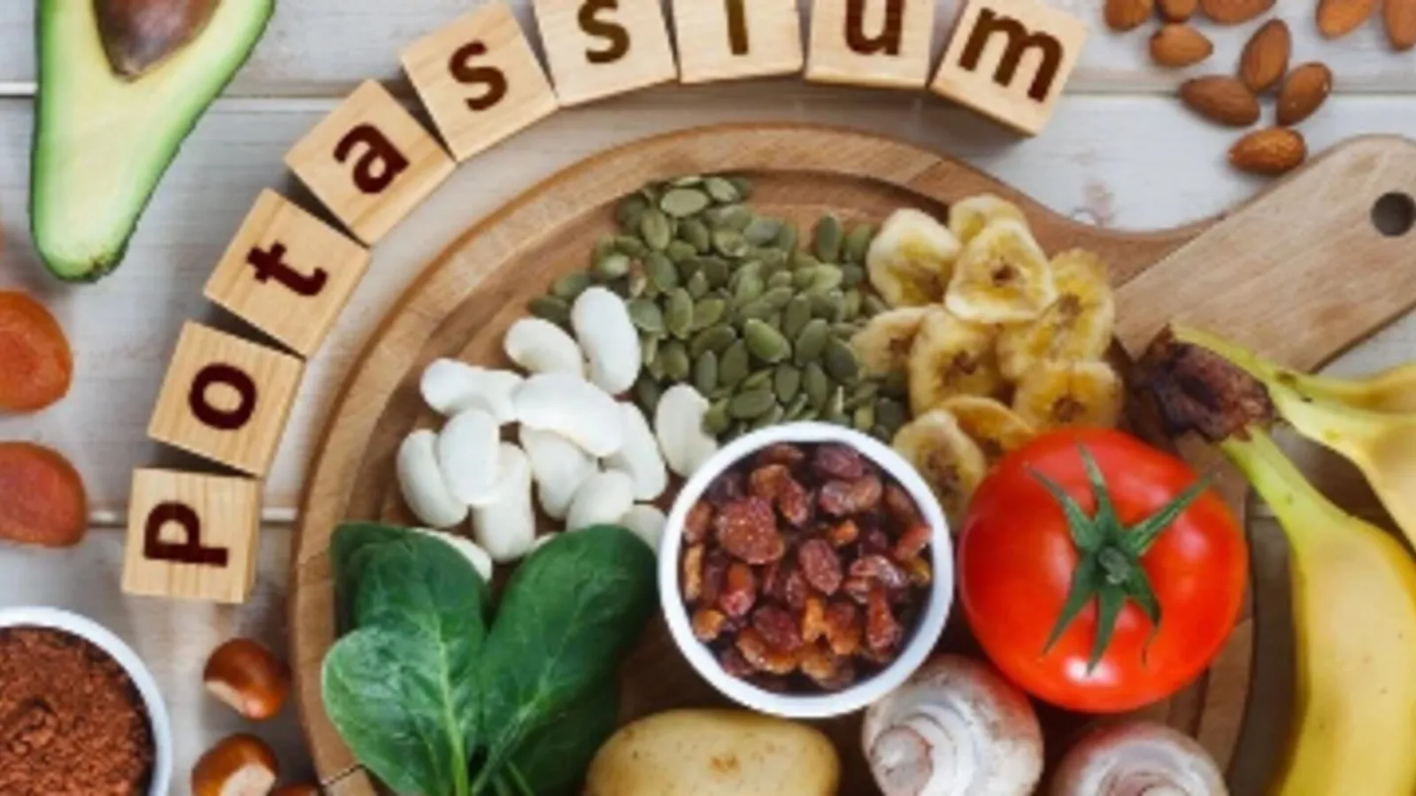 Tabla de madera con alimentos ricos en potasio: aguacate, plátano, espinacas, tomate, frutos secos y semillas